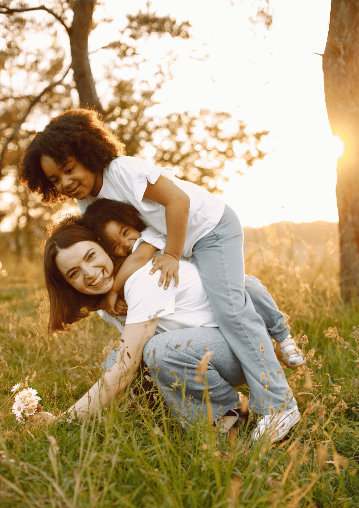 Photo d'une mère et de ses deux enfants jouant dans l'herbe à la tombée du jour